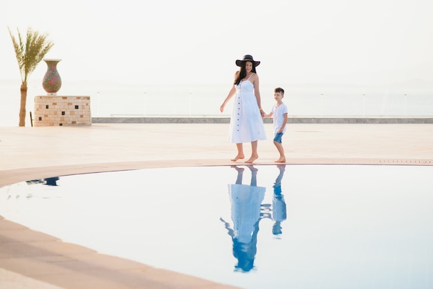 Young mother and son walking near swimming pool. 