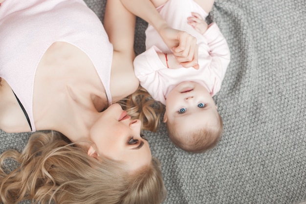 Young mother taking care of her little baby girl. Beautiful mom and her daughter indoors in the bedroom. Loving family. Attractive mum holding her child.