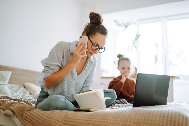 若い母親が電話で話し、子供の世話をしながら仕事の問題について話し合うCovid19