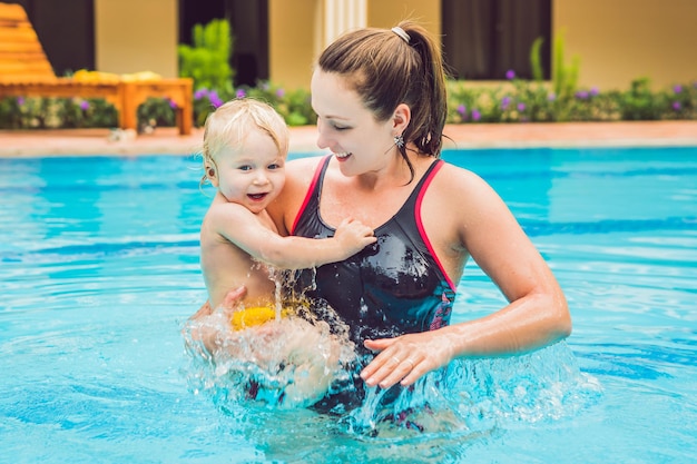 Молодая мама учит своего маленького сына, как плавать в бассейне