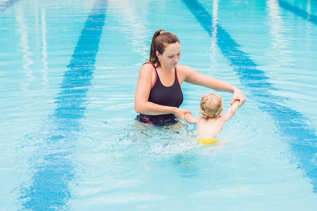 Young mother teach her little son, how to swim in a swimming pool