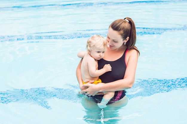 Молодая мама учит своего маленького сына, как плавать в бассейне