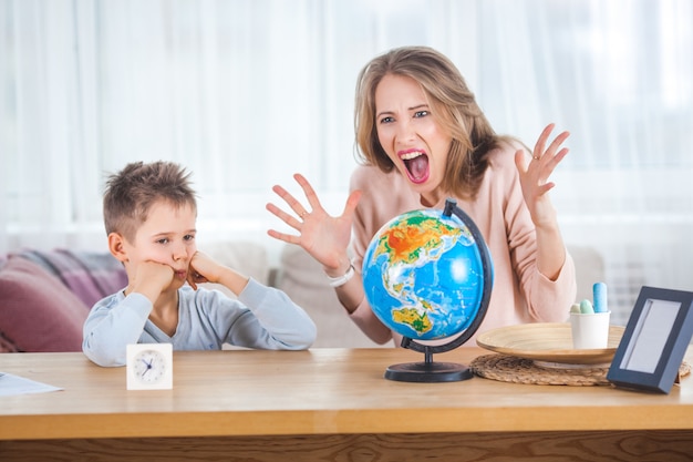 Young mother teaching her little son at home. Mom and her child studing geography indoors