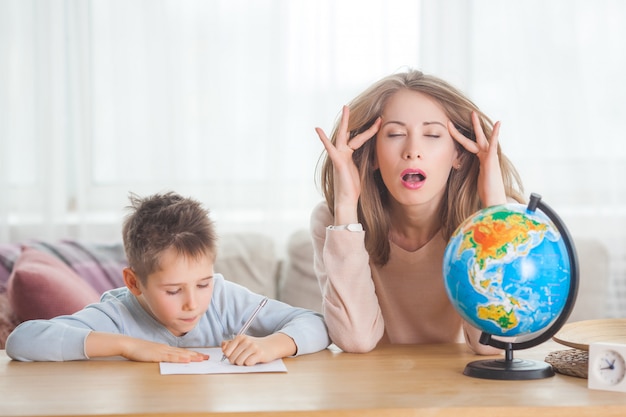 Young mother teaching her little son at home. Mom and her child studing geography indoors