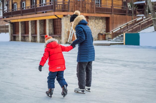 Young mother teaching her little son ice skating at outdoor skating rink Family enjoy winter on icerink outdoors