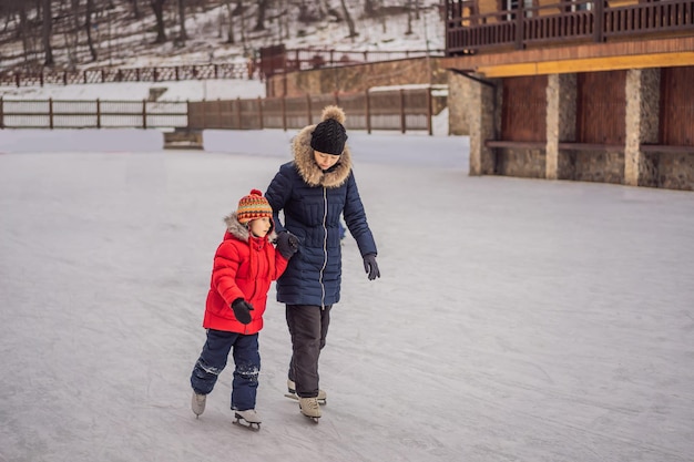 Young mother teaching her little son ice skating at outdoor skating rink Family enjoy winter on icerink outdoors