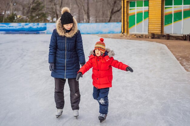 young mother teaching her little son ice skating at outdoor skating rink Family enjoy winter on icerink outdoors