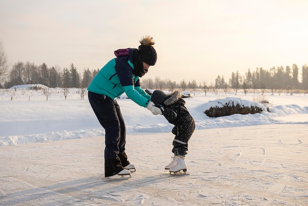 若い母親が息子にアウトドアスケート場でアイススケートを教えています 家族はアイススケート場で冬を楽しんでいます