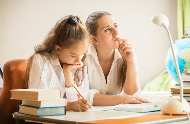 Photo young mother trying to solve complicated exercise with little daughter