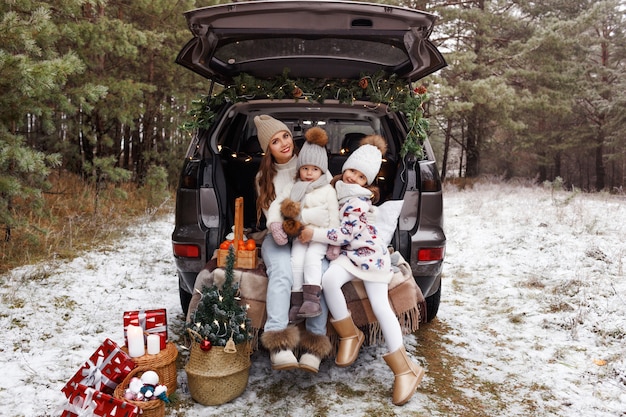 Photo a young mother and two little girls sit in the trunk of a car