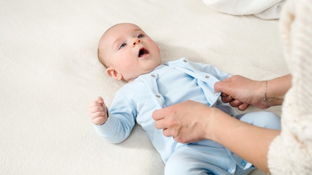 Photo young mother undressing and taking off clothes of her little baby son concept of parent baby hygiene