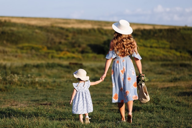 Young mother walking with her little daughter in the green field. Happy Mothers Day. Close up.