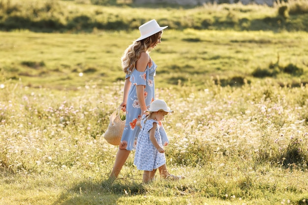 Молодая мать гуляет с маленькой дочерью в зеленом поле.