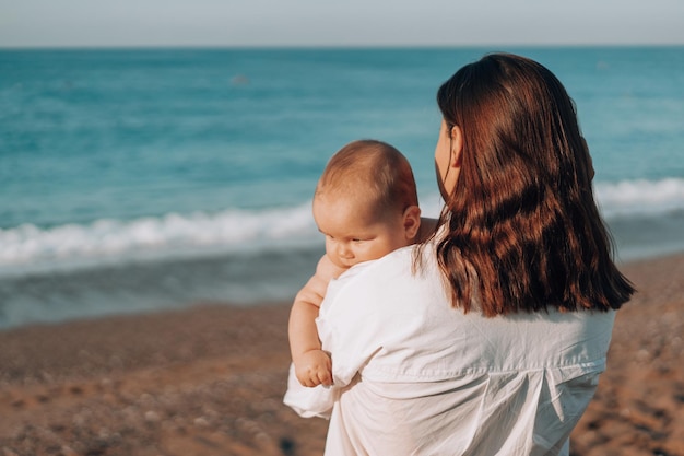 A young mother walks along the beach with a small child in diapers