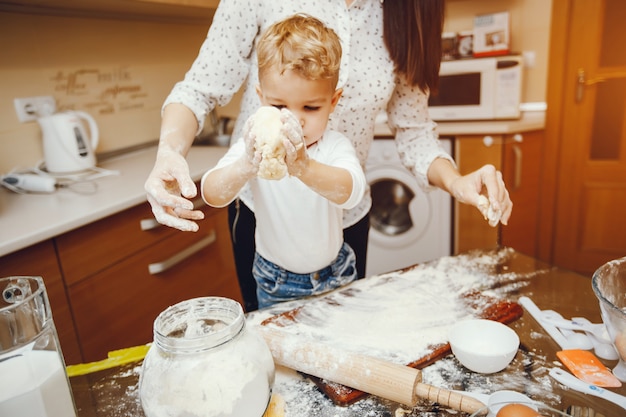 young mother in a white shirt preparing food at home in the kitchen with her little son