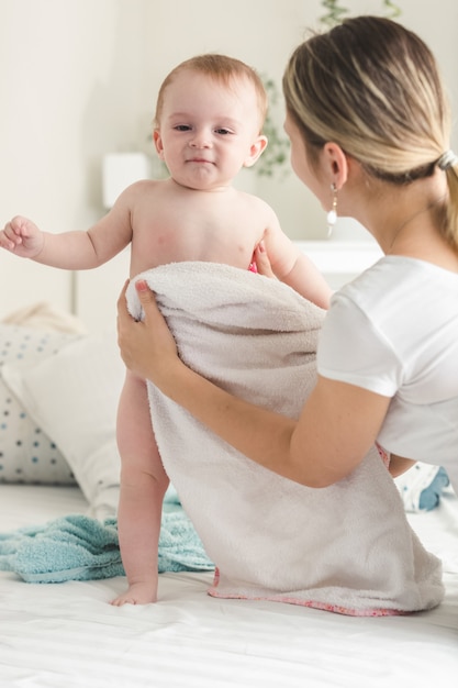 Photo young mother wiping her baby boy with towel on bed