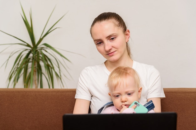 赤ちゃんを持つ若い母親がモニターを見てください。子供にコンピュータを害する