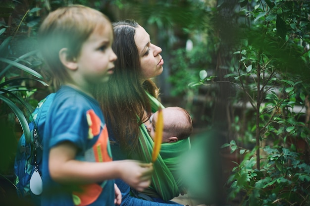 A young mother with a baby in a sling and little boy is walking in the jungle