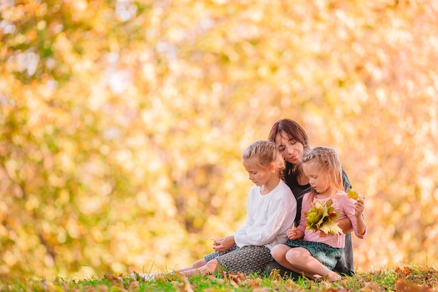 Young mother with cute little girls in autumn park on sunny day. Family enjoy warm weather at september day