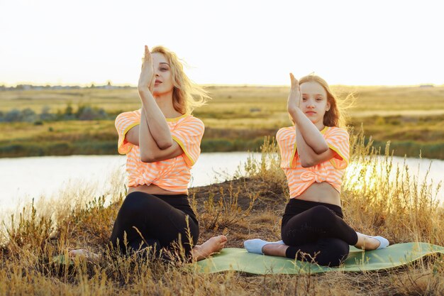 Young mother with daughter making yoga outdoors