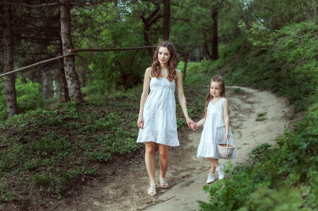 Young mother with her daughter goes on a footpath in the woods