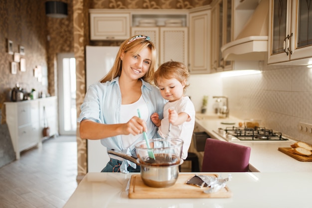 Young mother with her daughter mixing melted chocolate in a bowl.