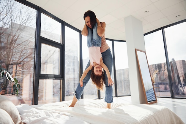 Young mother with her daughter spending weekend together on bed