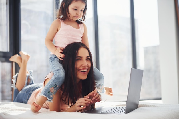 Giovane madre con sua figlia che trascorrono il fine settimana insieme in camera e utilizzano il laptop