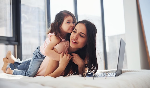 Young mother with her daughter spending weekend together in room and using laptop