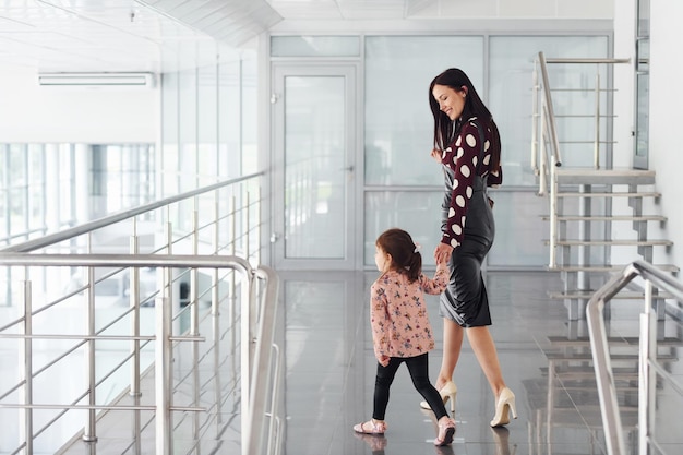 Young mother with her daughter walking together indoors in the office or airport Having vacation