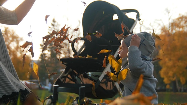 写真 秋の公園で空中に葉を投げる小さな赤ちゃんを持つ若い母親