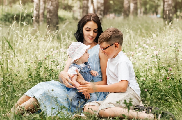 A young mother with her son and daughter sit on the grasses in the park