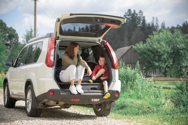 Young mother with kid boy sitting in car trunk resting in summer sunny day