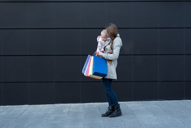 손에 팔과 쇼핑백에 작은 딸과 함께 젊은 어머니