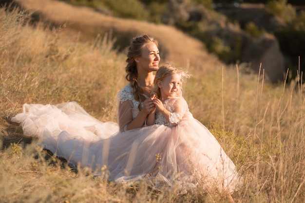 핑크 드레스에 작은 딸과 함께 젊은 어머니는 필드에 앉아있다. 엄마는 딸을 안고 포옹
