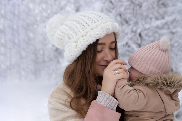 小さな子供を持つ若い母親が雪の中で遊ぶ