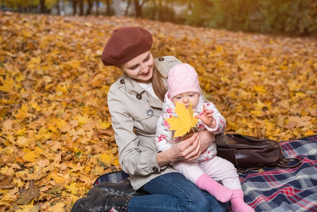 Young mother with small child sitting on picnic blanket on autumn Park background