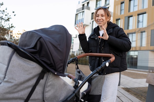 A young mother with a smile entertains her baby in a pram while walking on the street