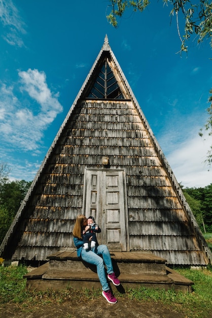 Young mother with son Happy mom kisses baby in nature on the background of an old wooden architectural house