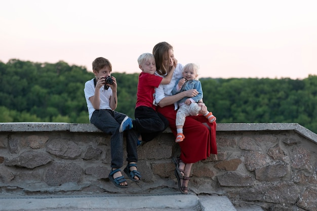 3人の子供を持つ若い母親が森の近くで休んでいます。子供と一緒に旅行する。幸せな家族。