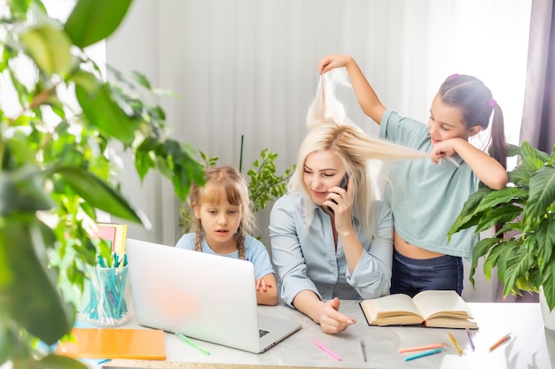 Una giovane madre con due bambini lavora da casa al computer. fatica stile di vita casalinga freelance. mamma stanca e due figlie piccole