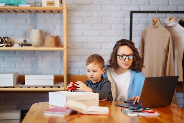 Young mother works with little boy business woman talking on\
the phone and discussing work issues