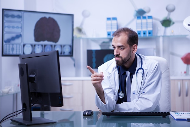 Photo young and motivated doctor pointing at his computer monitor. doctor concentrating on work.