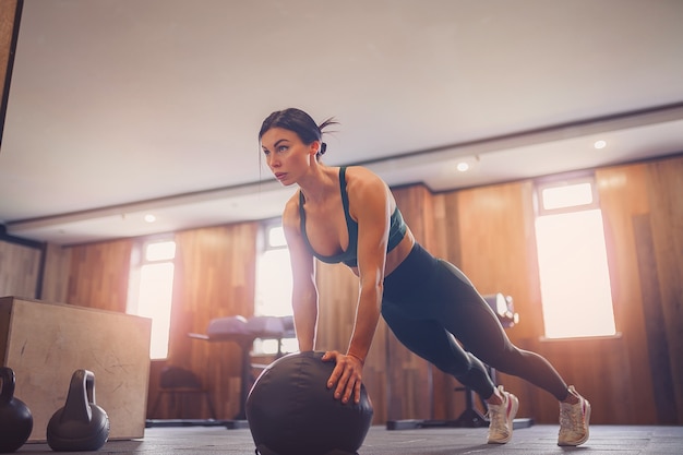 Young motivated girl doing plank exercise on ball at gym