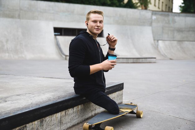 Ragazzo disabile giovane e motivato con una tazza di caffè prima di andare in longboard in uno skatepark