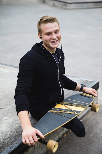 Молодой и целеустремленный парень с ограниченными возможностями с лонгбордом в скейтпарке
