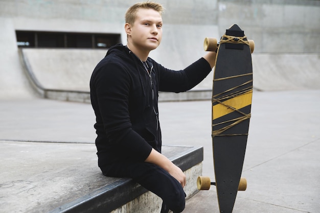 Ragazzo disabile giovane e motivato con un longboard in uno skatepark