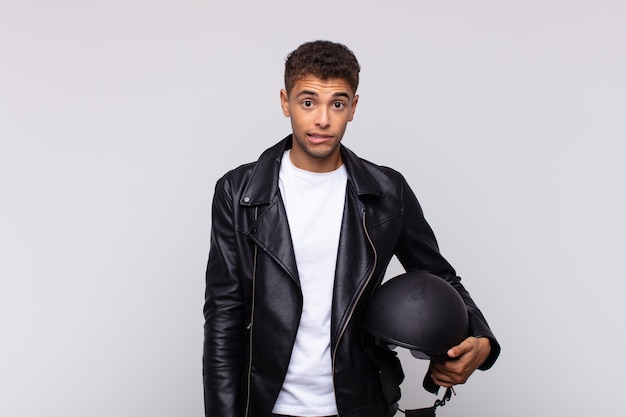 Young motorbike rider looking puzzled and confused, biting lip with a nervous gesture, not knowing the answer to the problem