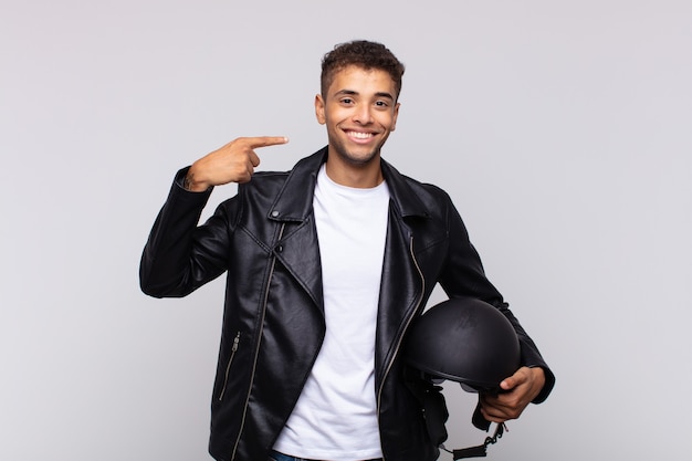 Young motorbike rider smiling confidently pointing to own broad smile, positive, relaxed, satisfied attitude