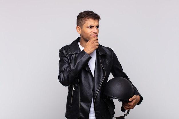 Young motorbike rider thinking, feeling doubtful and confused, with different options, wondering which decision to make